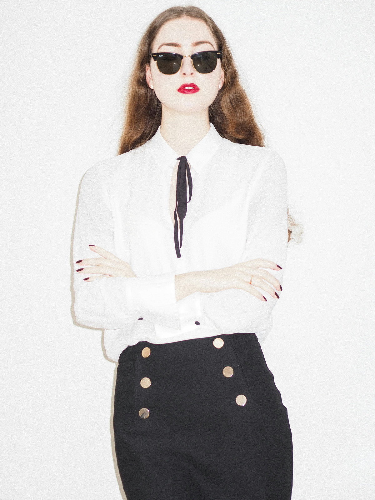 Woman wearing a black skirt with gold buttons paired with a white blouse and sunglasses