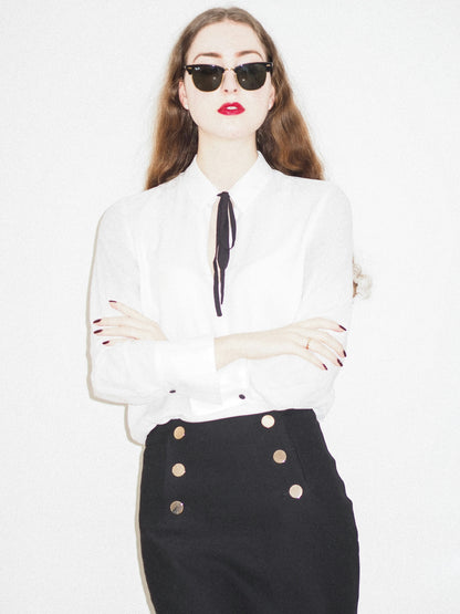 Woman wearing a black skirt with gold buttons paired with a white blouse and sunglasses