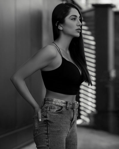 Woman wearing a black XAYWEAR crop top paired with high-waisted jeans and belt in side profile
