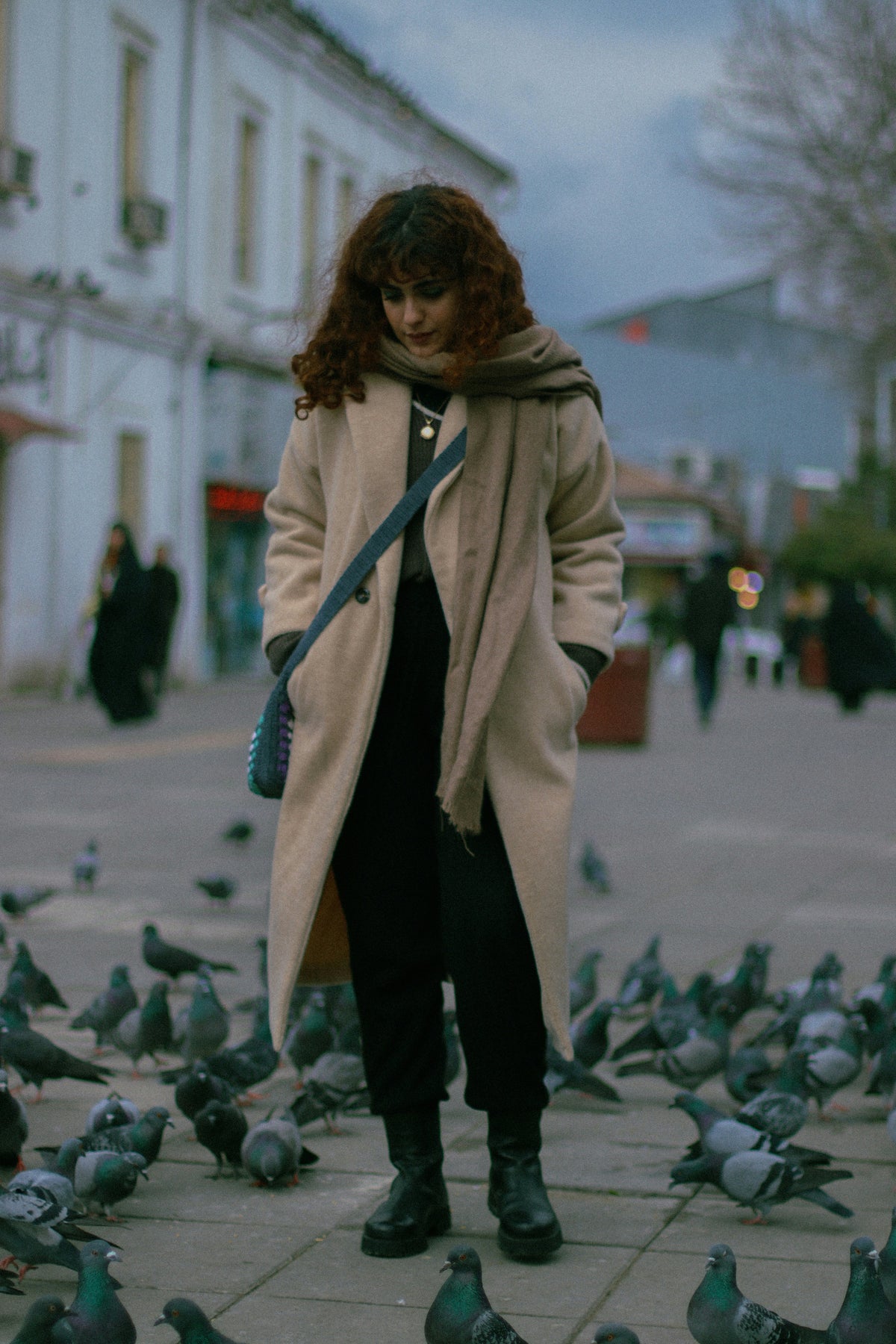 Elegant beige overcoat from XAYWEAR worn by a woman on a street surrounded by pigeons